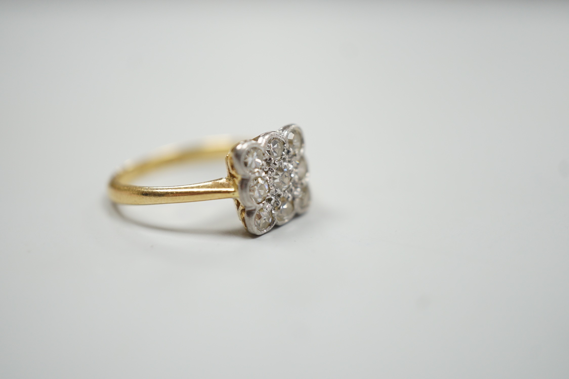 An 18ct and collet set nine stone diamond cluster table ring, size K/L, gross weight 2.6 grams.